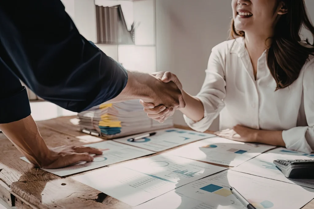 Billing company owner shaking hands with a healthcare client over revenue reports at a home office desk